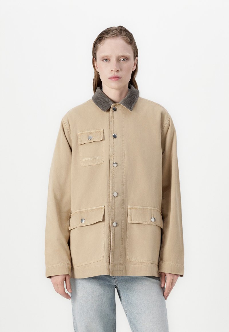 Bežová bavlněná bunda s kordovým límcem, dvěma předními kapsami, knoflíkovým zapínáním a uvolněným střihem. Obsahuje stříbrné kovové akcenty.