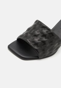 Chanclas negras con una parte superior texturizada y de diseño de punta cuadrada. El material parece suave con un ligero brillo.