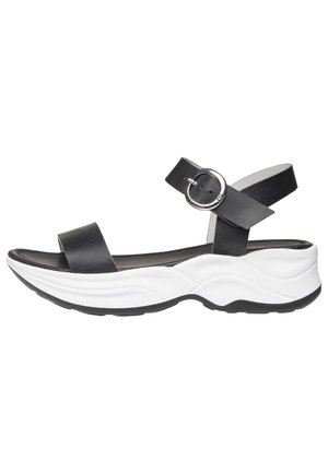 Sandale ouverte en cuir noir avec boucle de sangle réglable à la cheville et semelle contournée blanche épaisse, vue de côté.