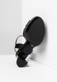 Scarpa nera in pelle con tacco curvo, punta aperta e cinturino regolabile. La suola è liscia con una leggera texture, che mette in evidenza il marchio italiano.