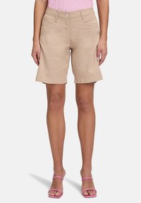 Shorts en coton beige avec une coupe décontractée, ourlet replié et deux poches avant. Assortis à des sandales roses à lanières.