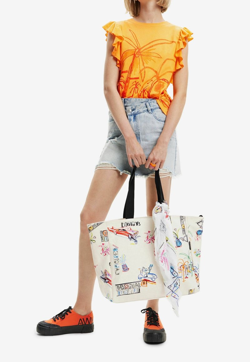 Femme portant un haut orange à motif de palmiers et une jupe en jean, tenant un grand sac blanc avec des dessins griffonnés colorés.