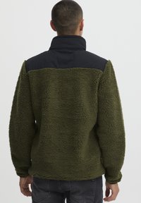 Green fleece pullover with a black nylon yoke, featuring a high collar and textured surface. Loose fit and long sleeves.