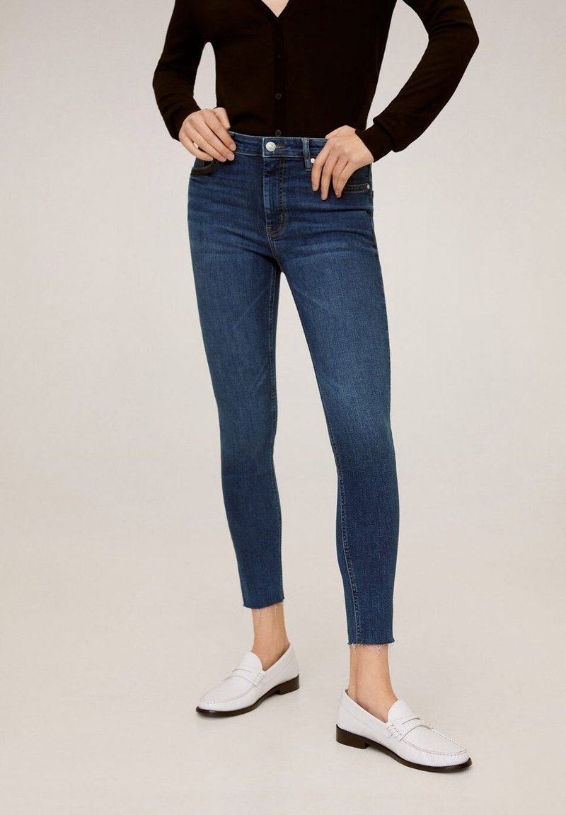 Jeans blu skinny in denim, con vita alta, orlo sfilacciato e silhouette aderente; abbinati a mocassini bianchi.
