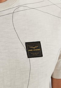 Korte mouwen, lichtgrijze T-shirt van textuurstof, zwarte stiksels en een vierkante, gestikte label met de tekst "PME Legend."