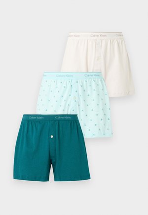 Drei Calvin Klein Herren-Boxershorts in Creme, Hellblau mit Logo-Muster und Dunkel-Türkis, übereinander auf weißem Hintergrund angeordnet.