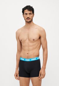 Black boxer briefs with a blue Puma logo waistband, featuring a snug fit and smooth texture for comfort. Model shown without a shirt.