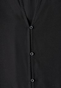 Gros plan sur un tissu de chemise noire avec trois petits boutons noirs alignés verticalement sur le devant de la patte de boutonnage.