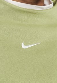 Grön idrottströja i stickad tyg, med en vit Nike-logotyp. Kragen är vit, och strukturen verkar slät och mjuk.