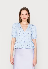 Blusa peplum azul clara em tecido suave, com decote em V, mangas curtas bufantes e padrão floral. Ataca-s ao lado para ajuste personalizado.
