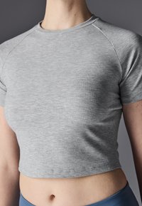 Sivi rebrasti cropped top s kratkim rukavima i okruglim izrezom. Tkanina je teksturirana, prilagođena tijelu i završava iznad struka.