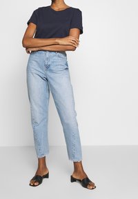Navy cotton t-shirt, high-waisted light blue jeans, and black slip-on block heel sandals. Jeans feature a relaxed fit and raw hem.