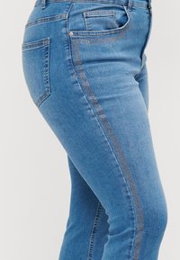 Vaqueros de mezclilla en azul claro, con un corte ajustado, sutiles acentos brillantes a lo largo de la costura lateral y un clásico diseño de cinco bolsillos.