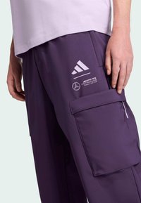 Paarse cargo broeken van gladde stof, met zijzakken, Adidas-logo en Mercedes-branding op de bovenbeen.