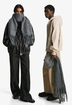 Grey wool scarf with fringed edges, paired with a black leather jacket, relaxed-fit beige hoodie, and dark wide-leg jeans.