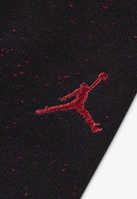 Chaussette en tissu noir avec des éclaboussures rouges ; présente un logo Jumpman rouge brodé en évidence. La texture est lisse, avec un design ajusté.