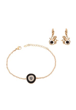 Złota bransoletka z łańcuszkiem z czarno-białym talizmanem w kształcie oka proroka, zestawiona ze złotymi kolczykami w kształcie czajniczków z czarnymi kamieniami.