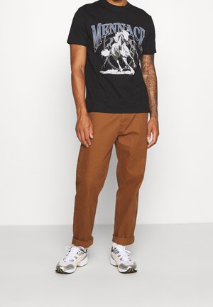 Black graphic t-shirt featuring a horse design, paired with brown pants and white sneakers with silver and gold accents.