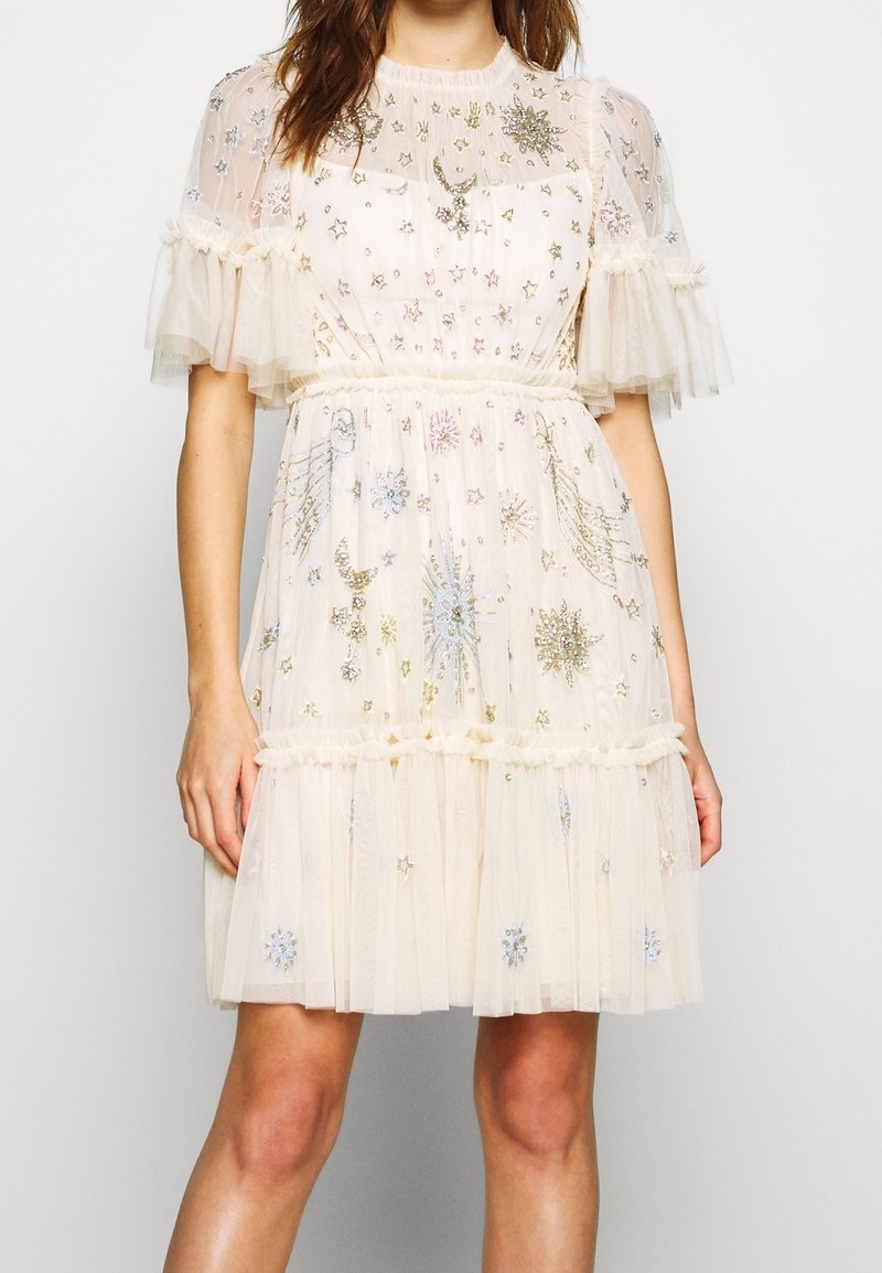 Tajt klänning i krämfärgad tyl med korta volangärmar. Har intrikata broderade stjärn- och blommönster med paljetter. Lagerkjol.