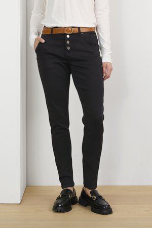 Pantaloni neri aderenti con chiusura a cinque bottoni e tasche frontali, abbinati a una cintura in pelle marrone. Tessuto testurizzato e design elegante.
