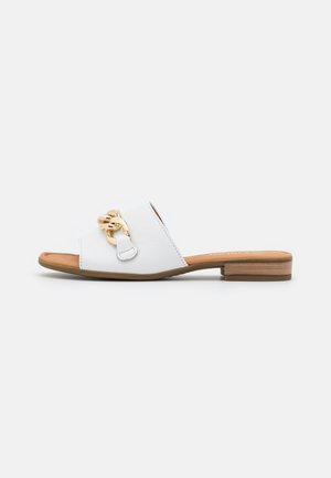 Biała skórzana sandałka typu slip-on z płaskim drewnianym obcasem i złotym łańcuszkiem na szerokim górnym pasku.