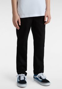 Schwarze Baumwollhosen mit schmaler Passform, kombiniert mit blau-weißen Sneakers mit Schnürdesign und kontrastierenden Akzenten.