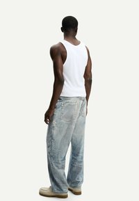 Bílý tílko bez rukávů, vybledlé modré džíny s opotřebovanými detaily a béžové tenisky. Džíny mají volný střih a několik kapes.