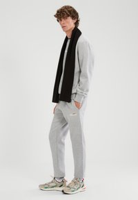 Szara bluza i spodnie dresowe z miękkiego materiału z małym logo, zestawione z wielokolorowymi sneakersami i czarnym szalikiem.