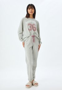 Harmaa loungewear-setti, joka sisältää pitkähihaisen paidan, kunnon "DREAM QUEEN 36" printillä ja yhteensopivat housut vaaleanpunaisella nauhalla, yhdistettynä vaaleisiin tossuihin.