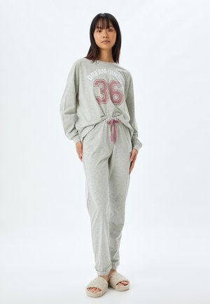 Graues Loungewear-Set bestehend aus einem Langarm-Oberteil mit dem Aufdruck "DREAM QUEEN 36" und passenden Hosen mit einem rosa Kordelzug, kombiniert mit beigen Hausschuhen.