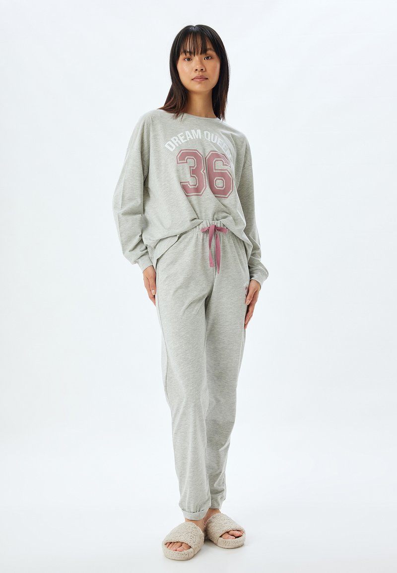 Harmaa loungewear-setti, joka sisältää pitkähihaisen paidan, kunnon "DREAM QUEEN 36" printillä ja yhteensopivat housut vaaleanpunaisella nauhalla, yhdistettynä vaaleisiin tossuihin.