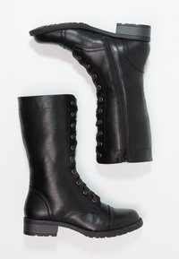 Botas de cuero negro hasta la rodilla con punta redondeada, cordones en la parte delantera y cremallera en el lateral. Presentan un tacón bajo y una suela texturizada.