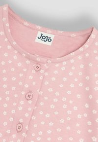 Prenda de algodón rosa con escote redondo, salpicada de pequeños patrones florales blancos. Presenta tres cierres de botones y una etiqueta que dice "JoJo."