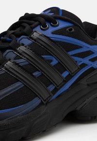 Svart och blå sportskor med mesh-övre del, tre svarta plastremsor, runda snören och strukturerad svart sula.