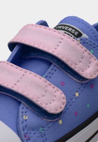 Μπλε παιδικό αθλητικό παπούτσι με παστέλ ροζ λουριά βέλκρο και πολύχρωμες πουά, που εμφανίζει μέρος του λογοτύπου Converse στη γλώσσα.