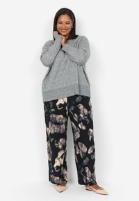 Pull en tricot gris à coupe ample, accompagné d'un pantalon noir à jambes larges orné d'un motif abstrait crème et gris. Des ballerines beiges complètent la tenue.