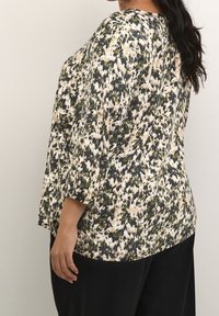 Løst siddende, mønstret bluse i en blanding af mørke, lyse og oliven grønne nuancer. Trekvartærmer med rund halsudskæring og glat tekstur.