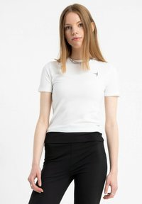 Biała koszulka z krótkim rękawem, uszyta z miękkiego materiału, z małym czarnym logo na piersi i dopasowanym fasonem. W połączeniu z czarnymi spodniami.