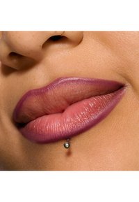 Gros plan sur des lèvres présentant un dégradé de nuances roses et violettes, avec un piercing labial métallique et une texture lisse. Aucun autre détail visible.
