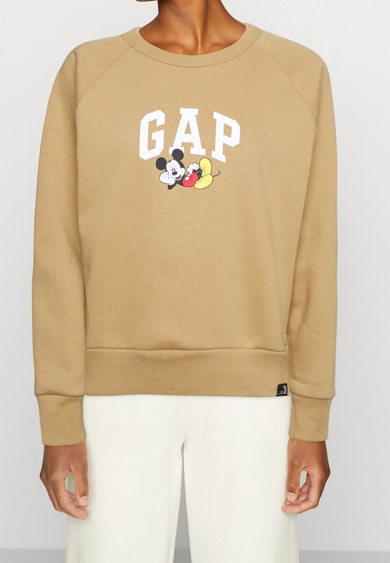 Brązowy sweter z białym napisem "GAP" i grafiką Myszki Miki. Wykonany z miękkiego materiału, z ściągaczami na mankietach i u dołu. Prosty design.