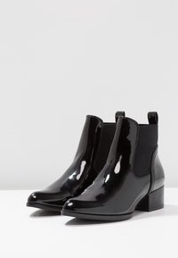 Bottes cheville en cuir verni noir avec panneaux élastiques sur les côtés, bout arrondi et talon carré. Fini brillant qui ajoute de l'éclat au design.