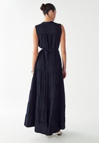 Čierne, bezrukávové maxi šaty s volánovým dizajnom a textúrovanou látkou. Úzky pás a splývavý silueta. Základný štýl bez ozdôb.