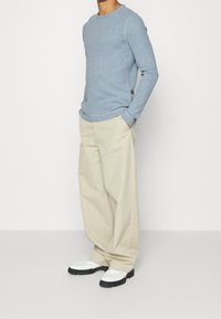 Světle modrá košile s dlouhým rukávem a kulatým výstřihem, doplněná volnými světle béžovými kalhotami a bílými botami s černými podrážkami.