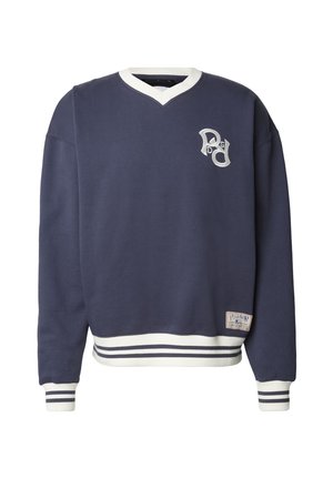 Tengerészkék V-nyakú pulóver, fehér díszítésekkel, bordázott mandzsettákkal és szegéllyel. A mellrészen hímzett logó, az alján pedig címke található.