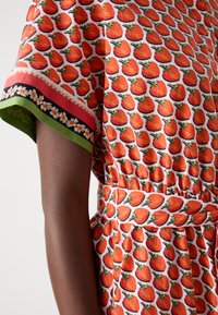 Kurzärmliges Kleid mit lebhaftem Erdbeer-Muster, tailliertem Schnitt, kontrastierendem Blumenbesatz und grünen sowie schwarzen Akzenten.