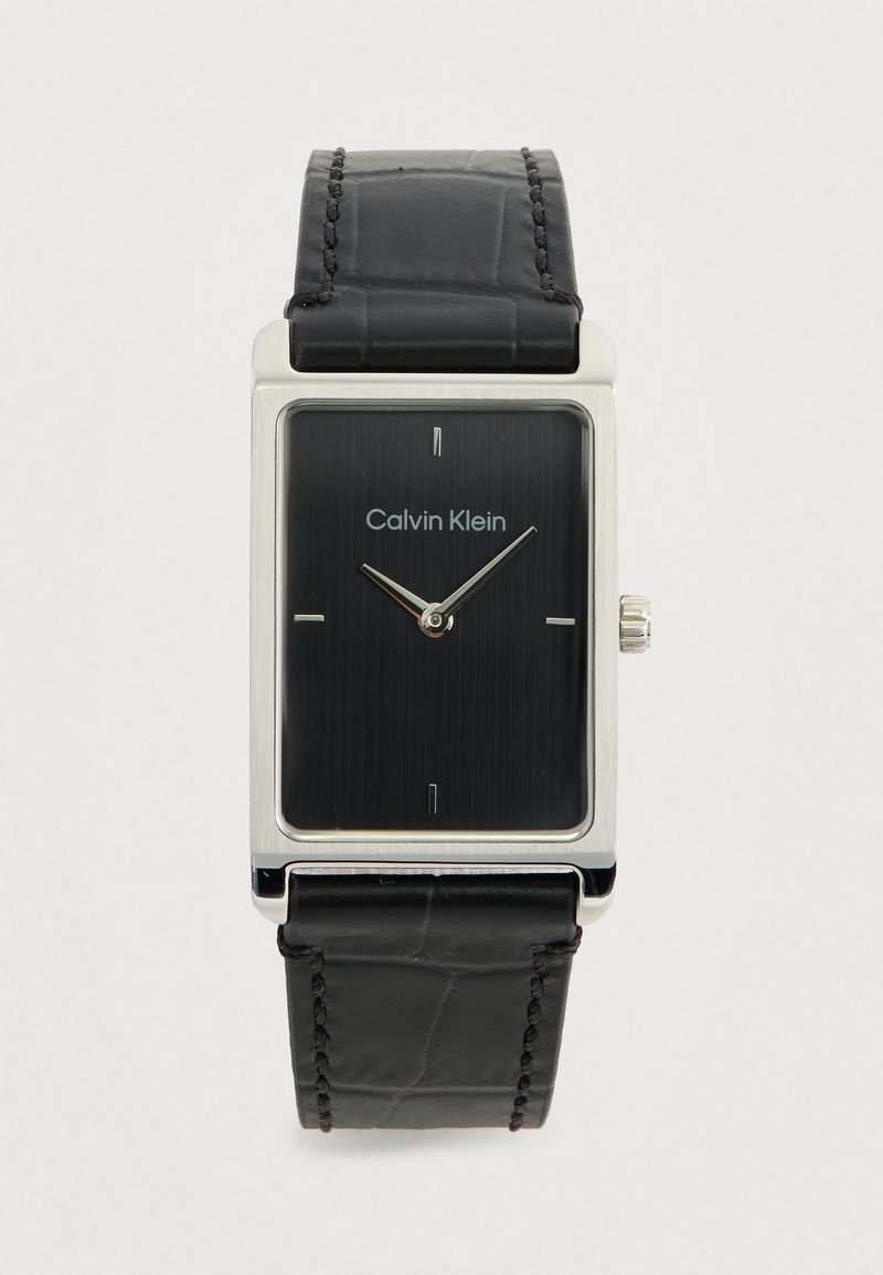 Montre rectangulaire Calvin Klein avec un cadran texturé noir, un boîtier en argent et un bracelet en cuir noir présentant des détails de couture subtils.