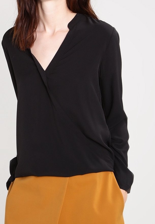 Schwarze Bluse mit langen Ärmeln, V-Ausschnitt und Falten-Details, kombiniert mit senfgelben Hosen. Glattes Material und lockere Passform.