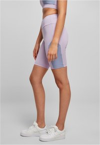 Lila Radshorts mit glatter Textur und einem kontrastierenden blauen Seitenpaneel. Kombiniert mit weißen Sneakers für einen sportlichen Look.