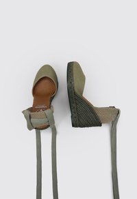 Espadrilles en toile verte avec un talon compensé, dotées d'une semelle en jute texturé et de liens de cheville réglables. Doublure en cuir visible.