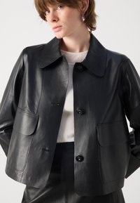 Črna usnjena jakna s krajšim krojem, s špicastim ovratnikom, dvema sprednjima žepoma in gumbnim zapiranjem. Gladka tekstura z elegantnim, minimalističnim dizajnom.